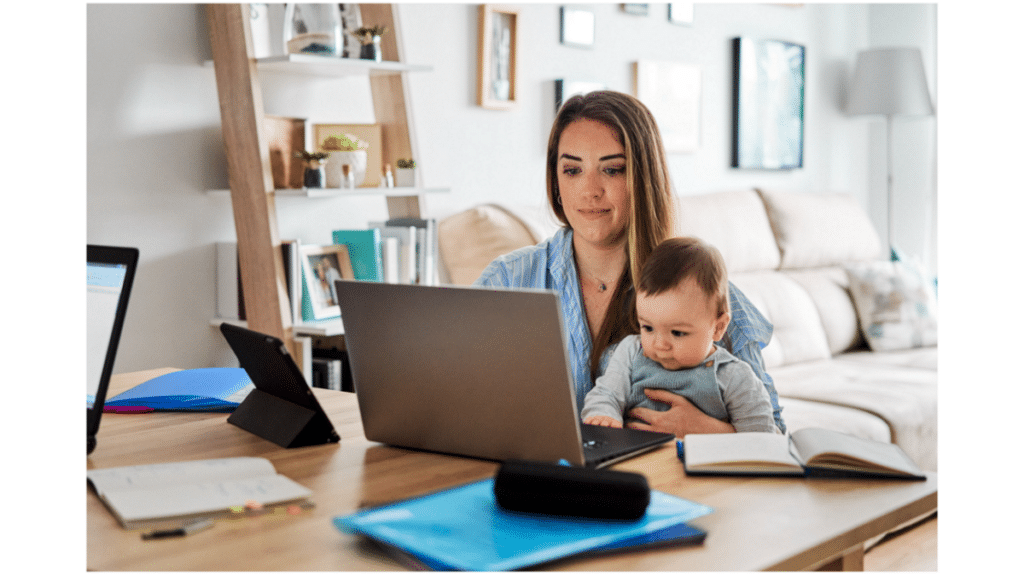 working parent sitting at their table working on their laptop while caring for a baby