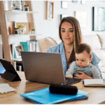 working parent and caregiver sitting at their table working on their laptop while caring for a baby