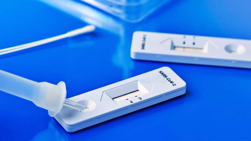 some workplace testing covid-19 rapid antigen test kits, with the diagnostic test devices and some nasopharyngeal swabs, on a blue surface