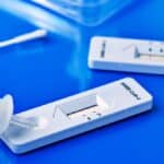 some workplace testing covid-19 rapid antigen test kits, with the diagnostic test devices and some nasopharyngeal swabs, on a blue surface