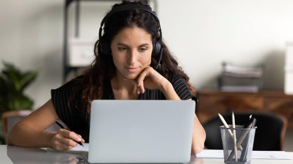Focused female adult in headphones using laptop, using HR Service Delivery on internet to improve employee experience